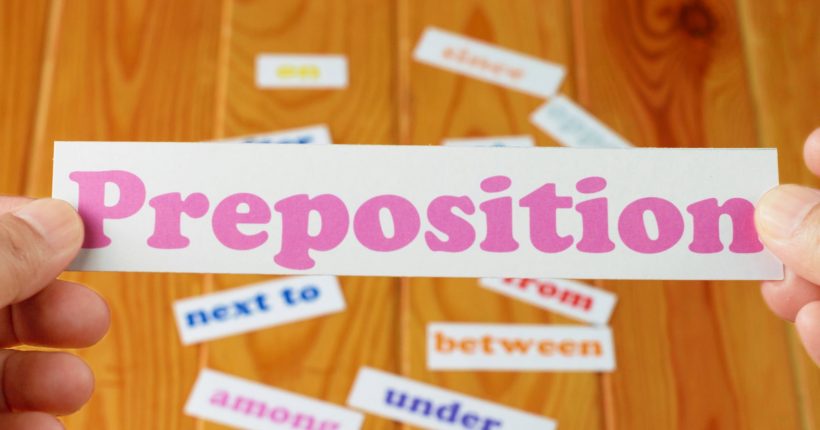 hand holding English preposition card over blurred preposition words on wooden table